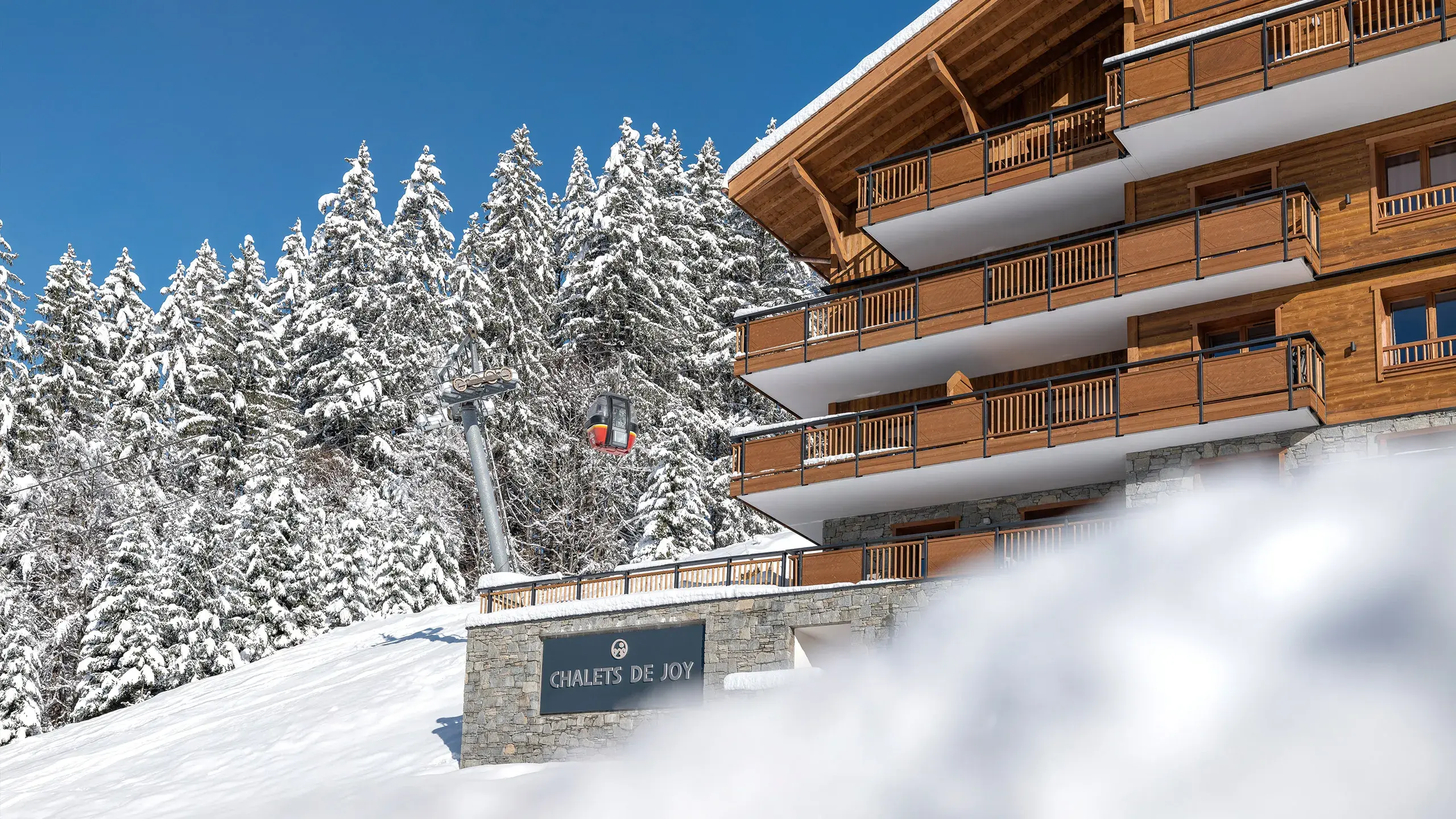 Vue extérieure des Chalets de Joy au Grand-Bornand en hiver, avec le télécabine de la Joyère