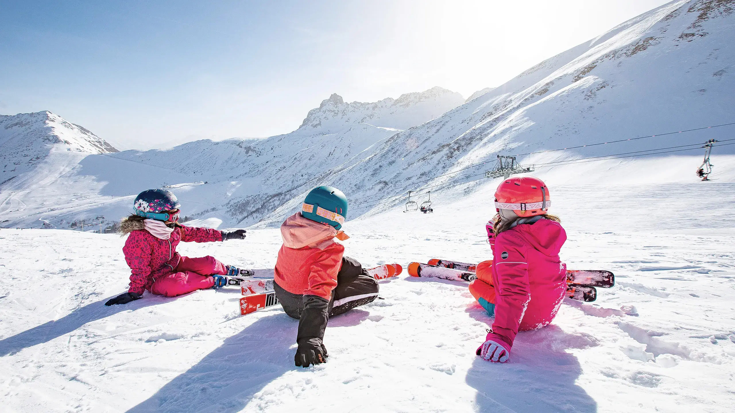 3 enfants à skis sont assis de dos et regardent la vue sur les pistes du Grand Domaine