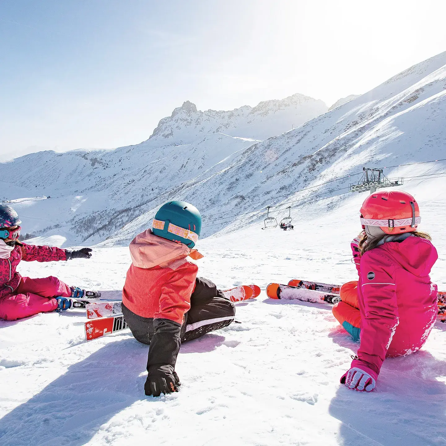 3 enfants à skis sont assis de dos et regardent la vue sur les pistes du Grand Domaine