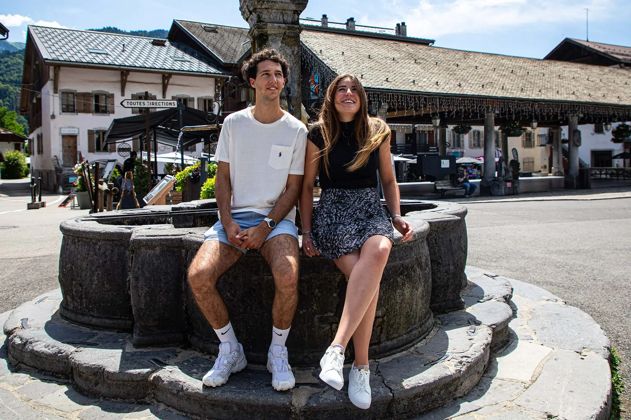 Un couple est assis sur le bord d'une fontaine dans le village de Samoëns