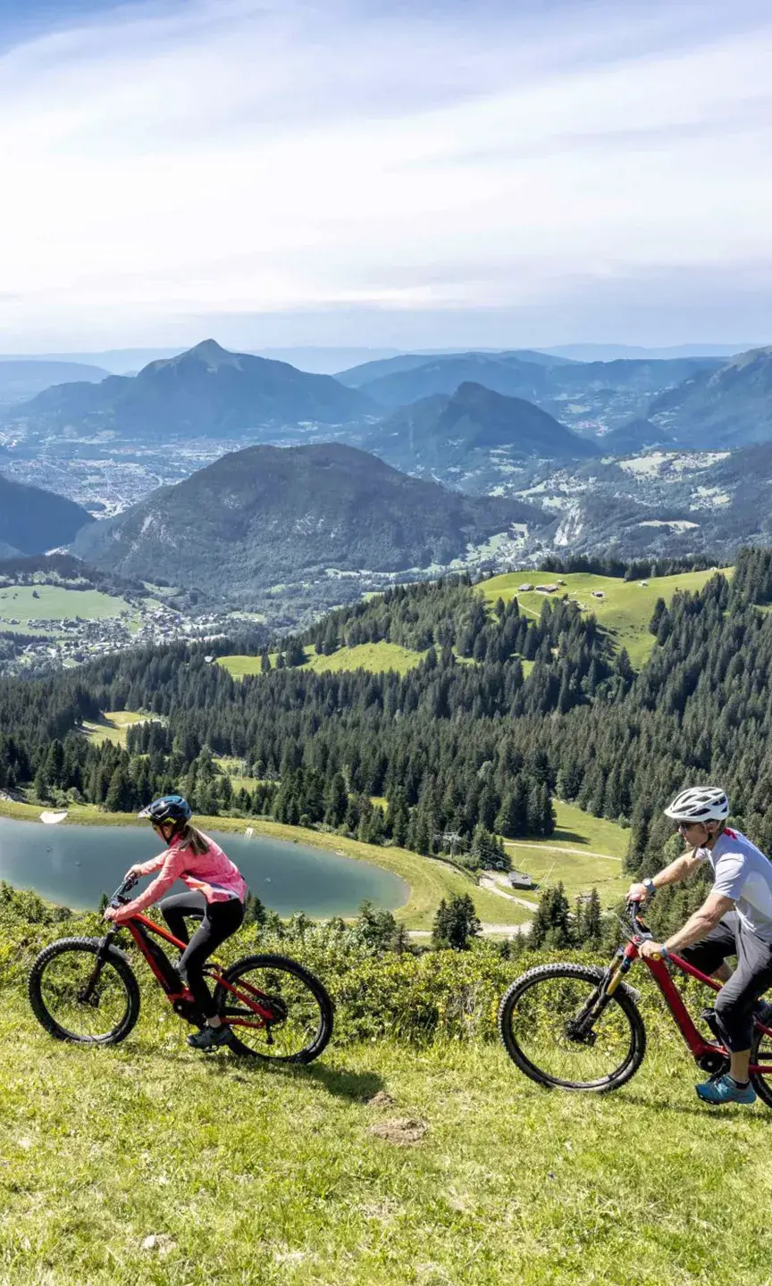 Une famille fait du vélo en été aux Carroz avec une belle vue sur les massifs environnants