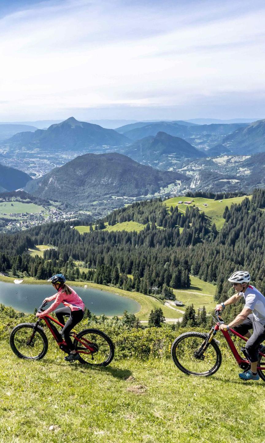 Une famille fait du vélo en été aux Carroz avec une belle vue sur les massifs environnants