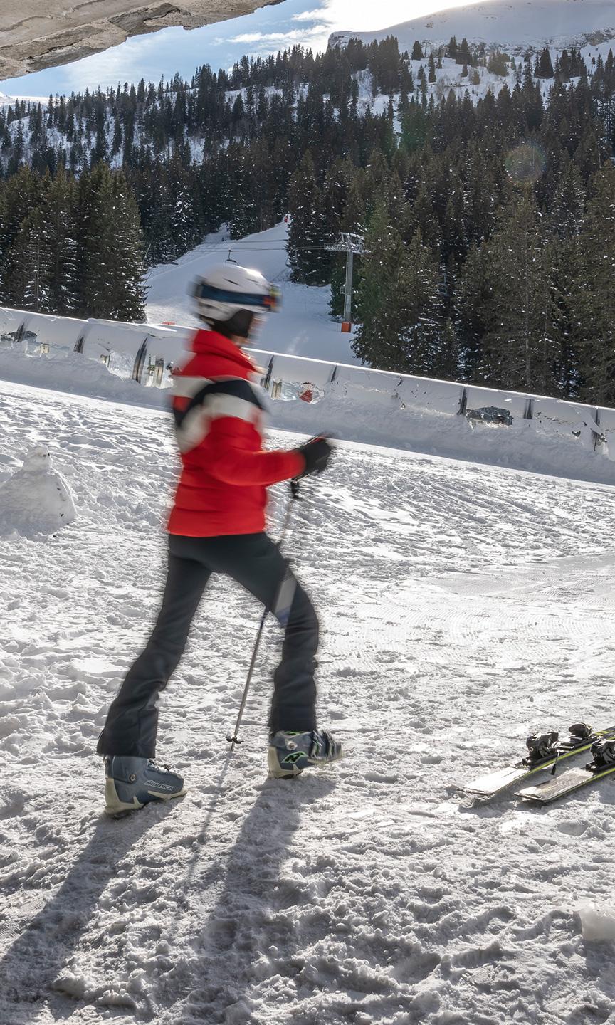 Femme qui chausse ses skis sur le front de neige de Flaine à la sortie du skiroom de la résidence Alhéna