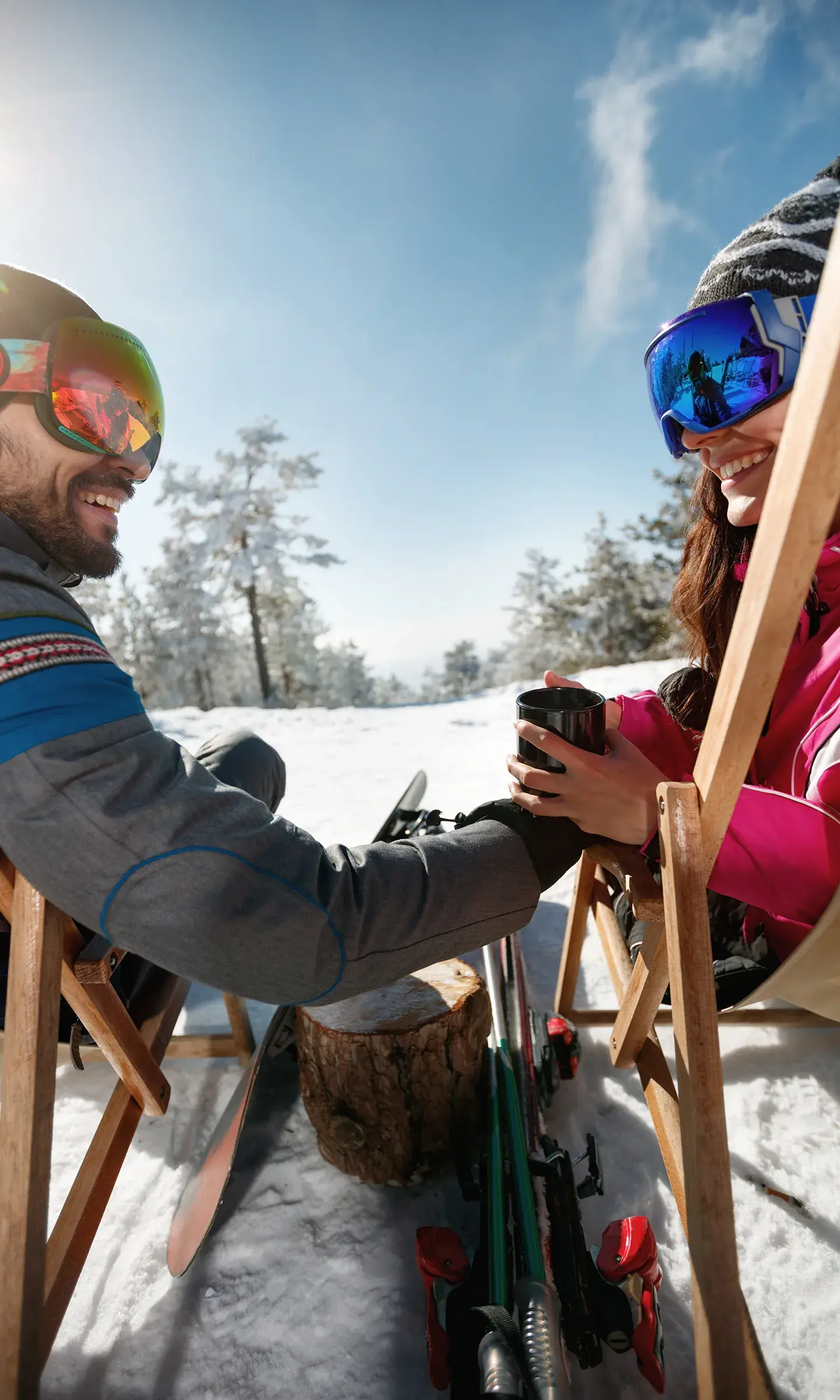 Un couple est en train de partager une boisson chaude confortablement installé sur les transats d'un bar sur des pistes enneigées