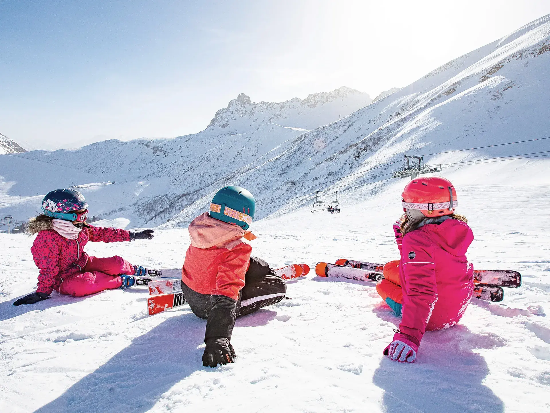3 enfants à skis sont assis de dos et regardent la vue sur les pistes du Grand Domaine