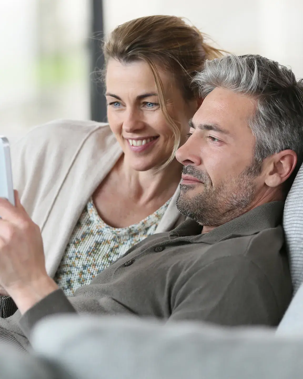 Un couple est en train de regarder quelque chose sur une tablette, assis sur leur canapé - Projet Investir à la montagne