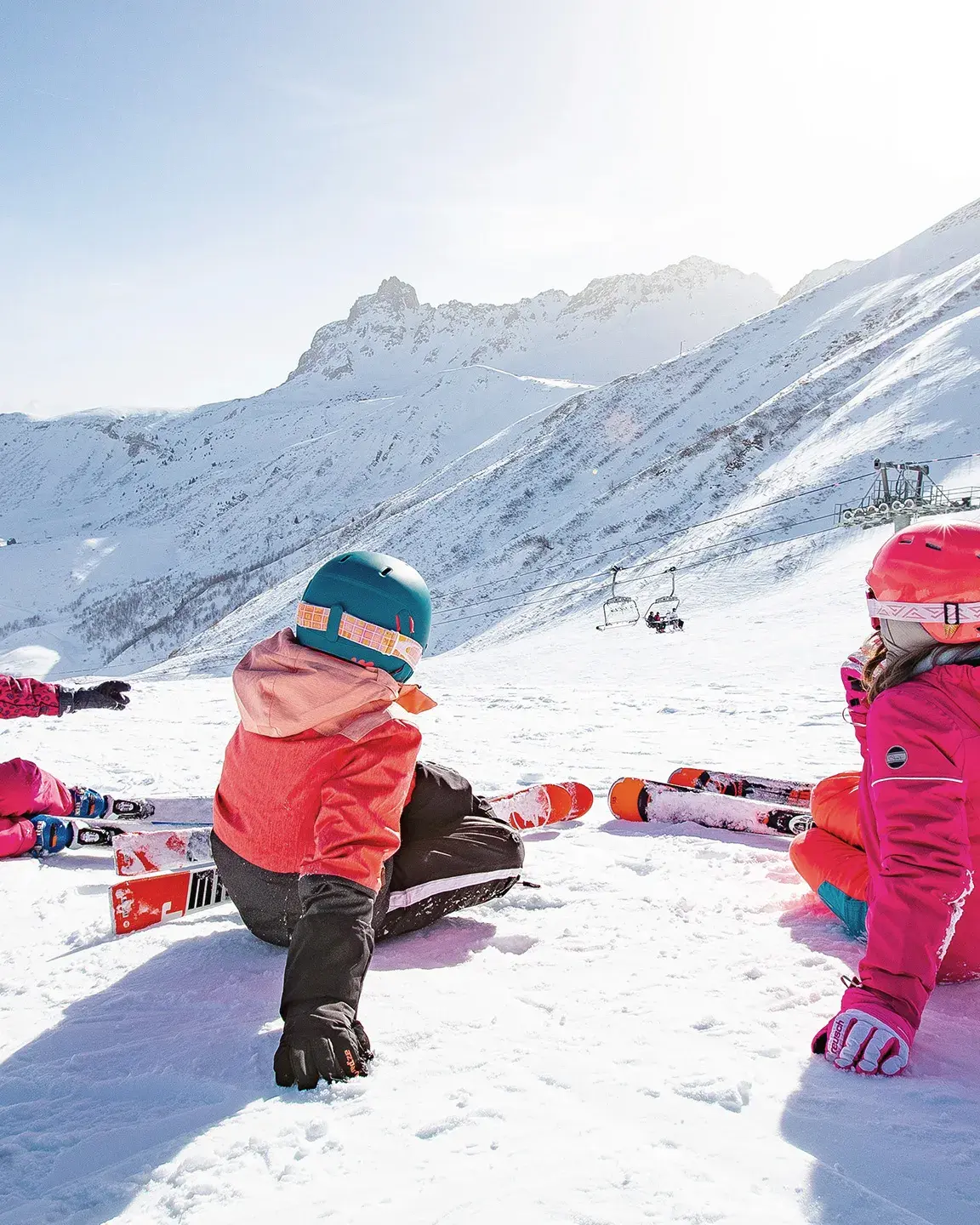3 enfants à skis sont assis de dos et regardent la vue sur les pistes du Grand Domaine
