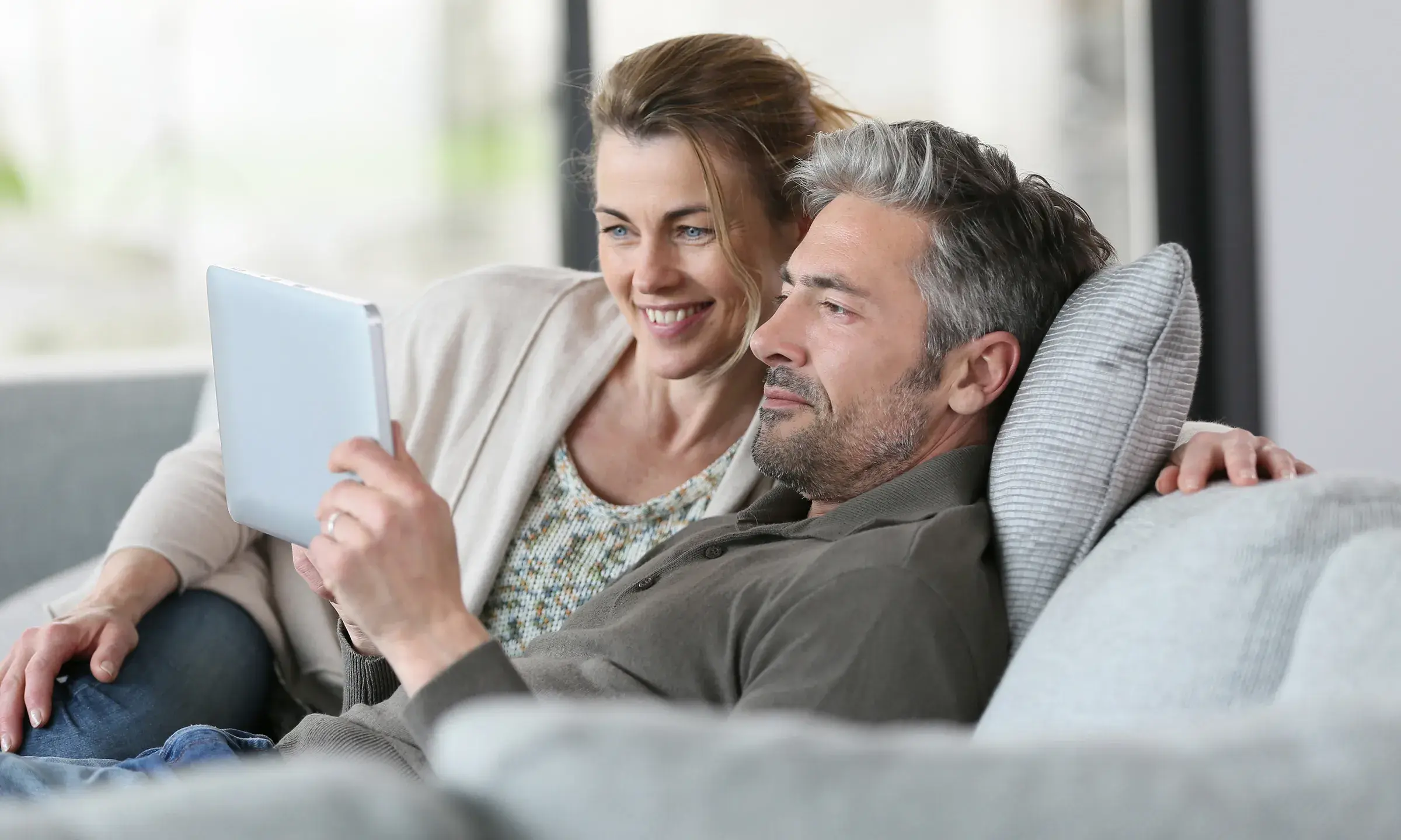 Un couple est en train de regarder quelque chose sur une tablette, assis sur leur canapé - Projet Investir à la montagne